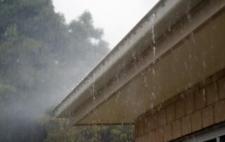Heavy rain pouring off a roof during a storm, highlighting potential drainage issues and roof vulnerability.